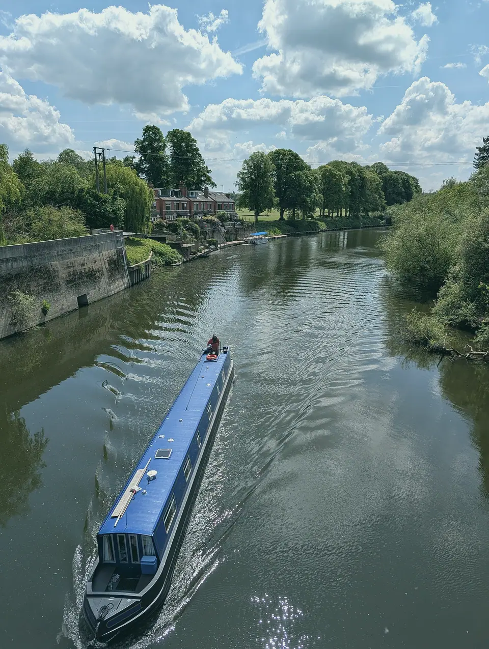 The roof of a blue narrowboat seen from above, cruising a wide stretch of river
