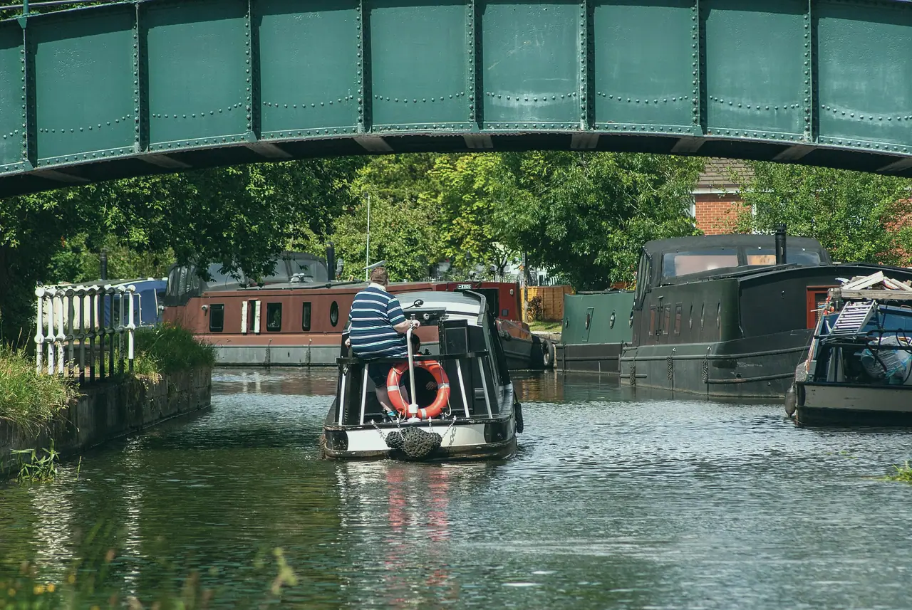 A narrowboat steered under a green iron bridge, a lifebuoy on the stern